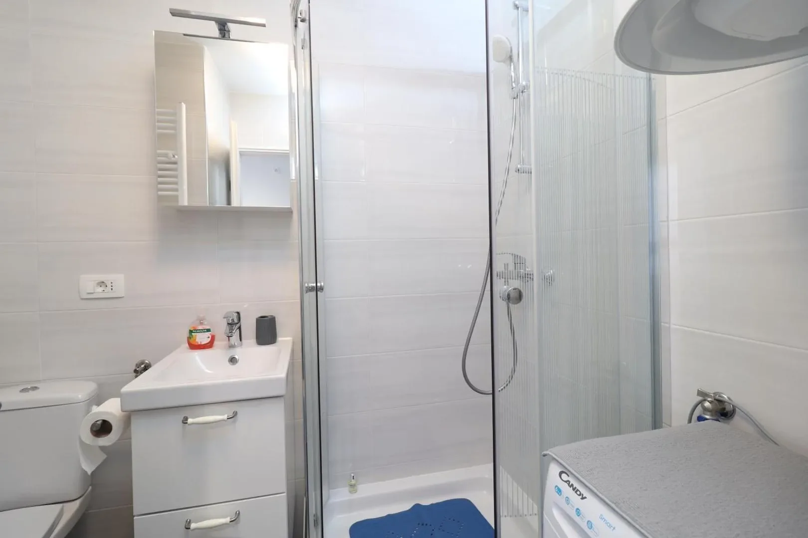 Bathroom with a glass shower enclosure, white vanity and washing machine.