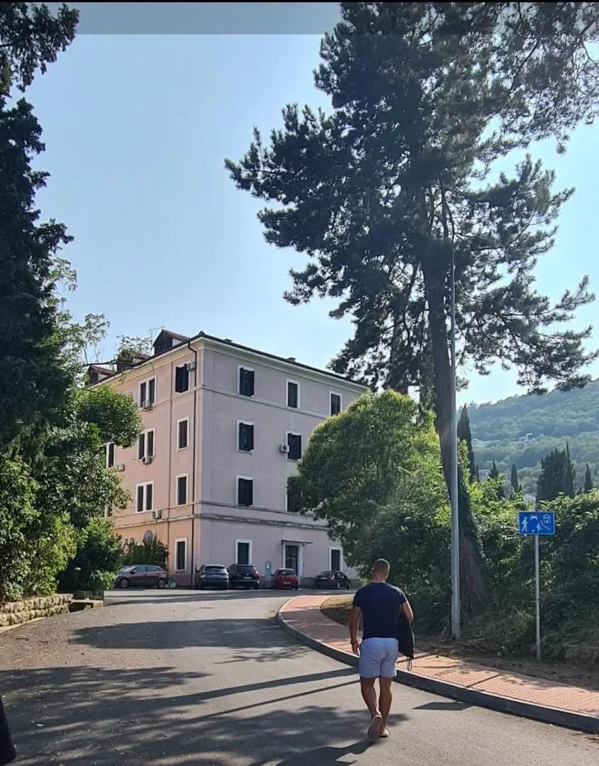 The apartment building on a sunny street, surrounded by trees and greenery.