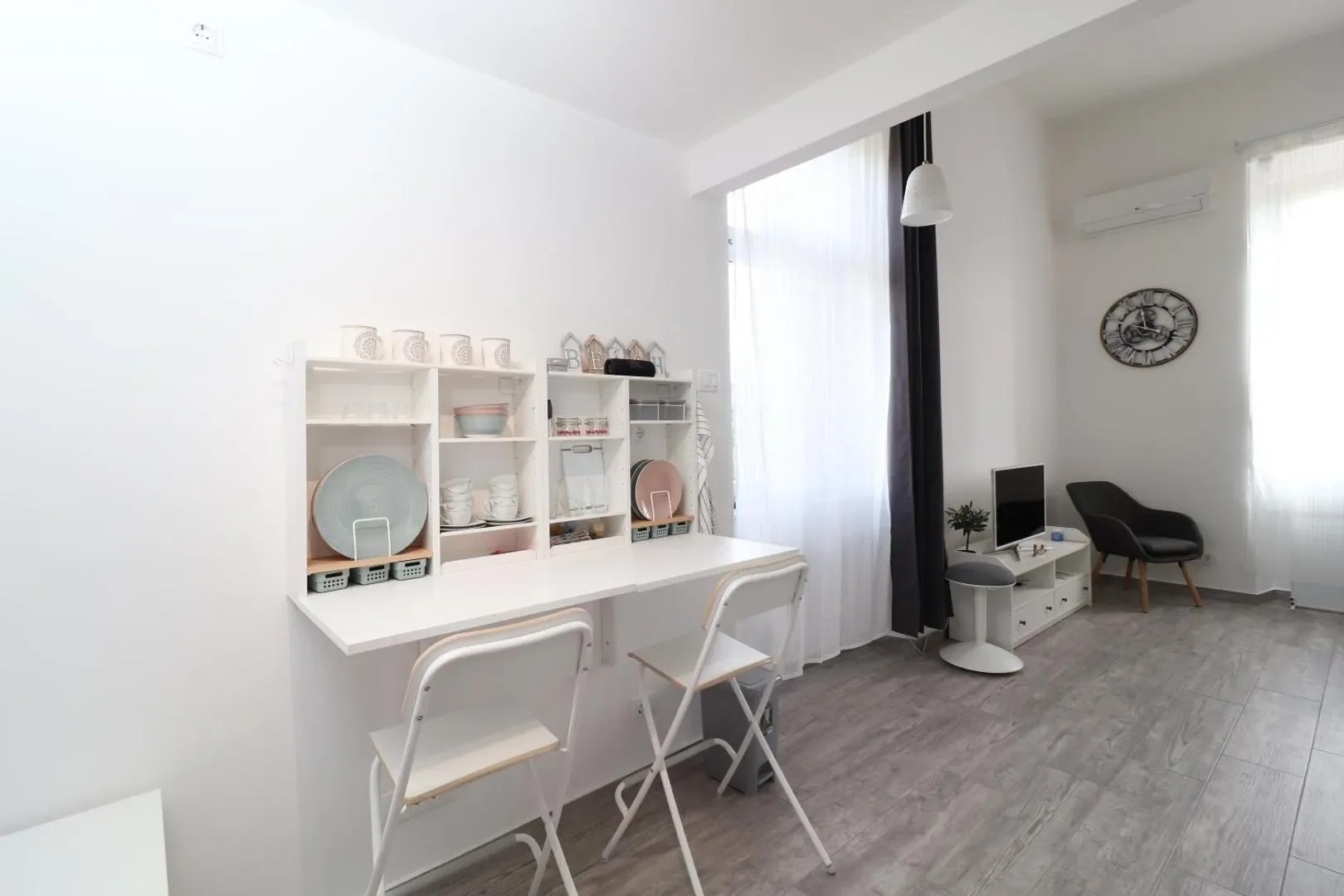 White dining counter and chairs with a view of the open living area and window.