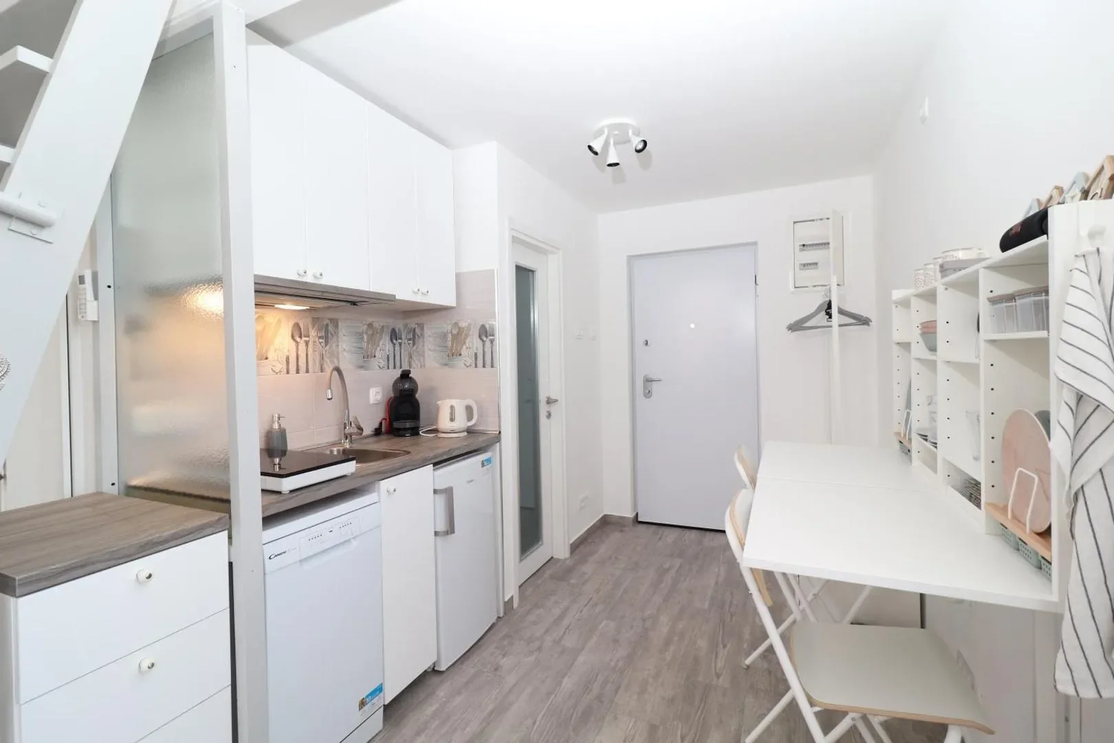 White kitchen beside a dining counter with two chairs in the open-plan apartment.