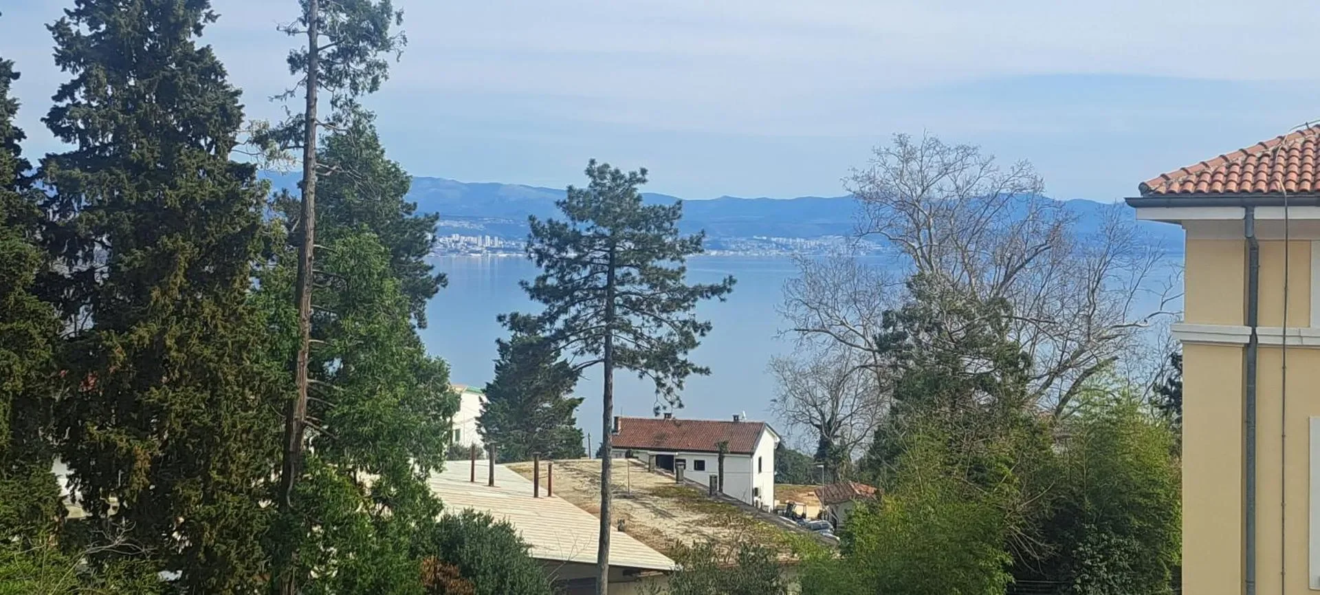 Kvarner Bay and the opposite coastline seen between trees and neighbouring rooftops.