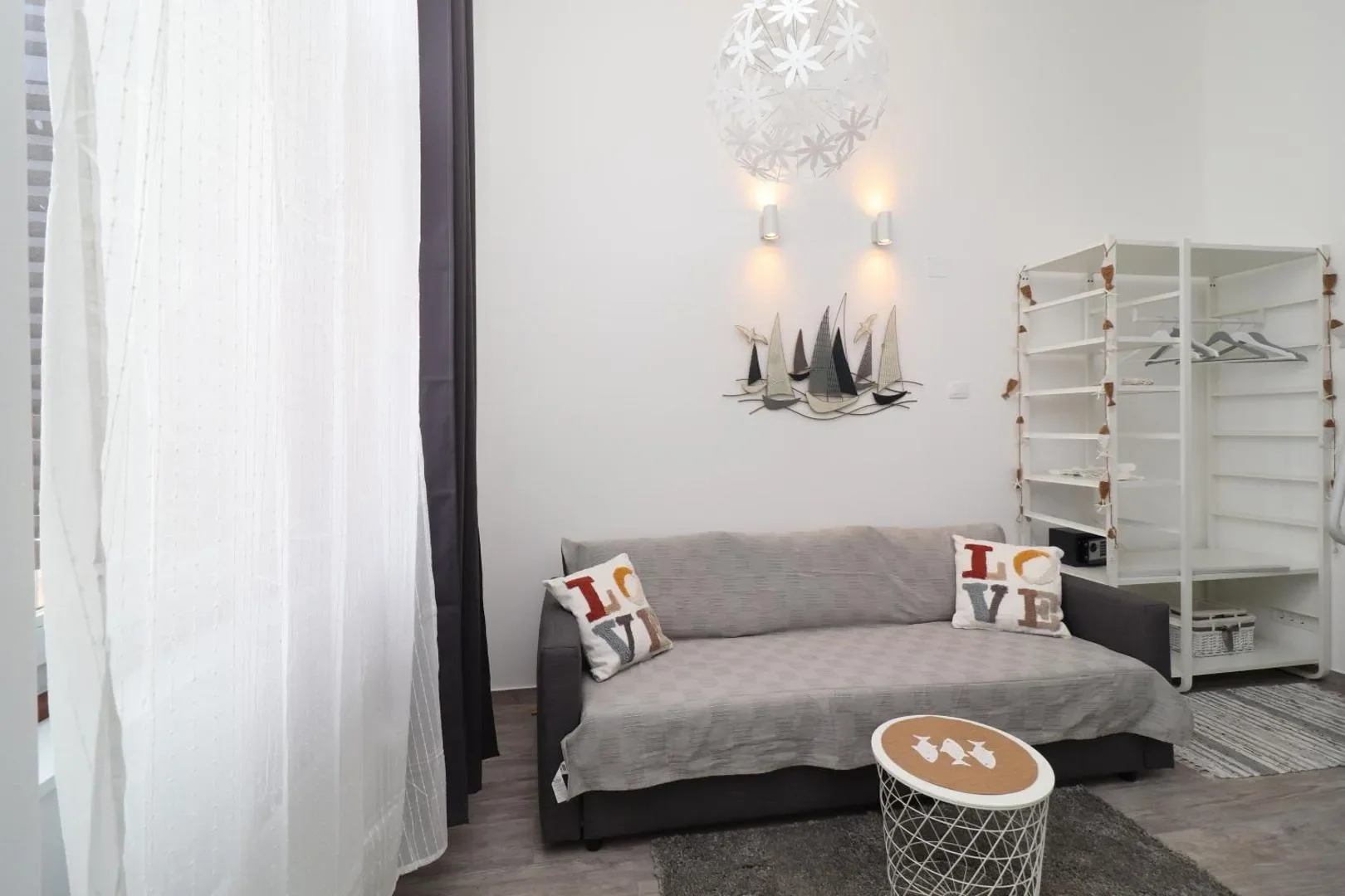 Grey sofa with cushions, a small round coffee table and open shelving beside the window.