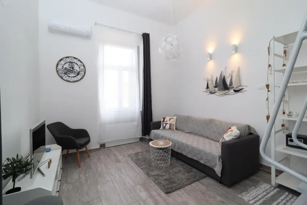 An overview of the open-plan studio, with a grey sofa, armchair, dining counter and large window